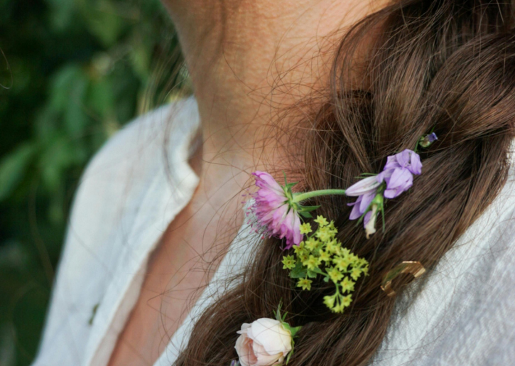 Lente haarvlecht met bloemen Gevlochten bruin haar versierd met kleine bloemen voor een frisse, lenteachtige uitstraling.